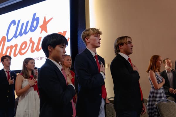 Charlie Kirk speaking at a podium with Turning Point USA branding in the background