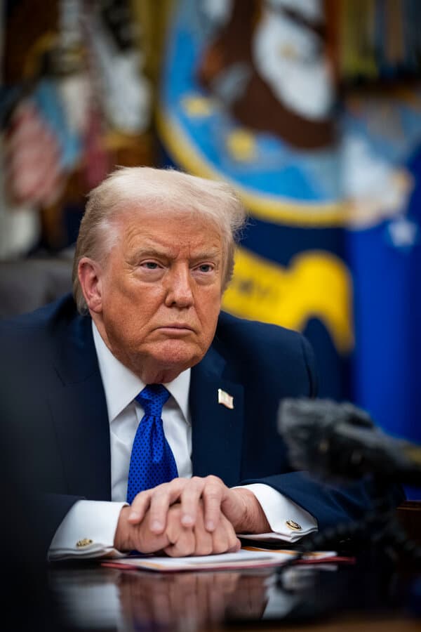 Donald Trump speaking at a podium with defense industry graphics in the background